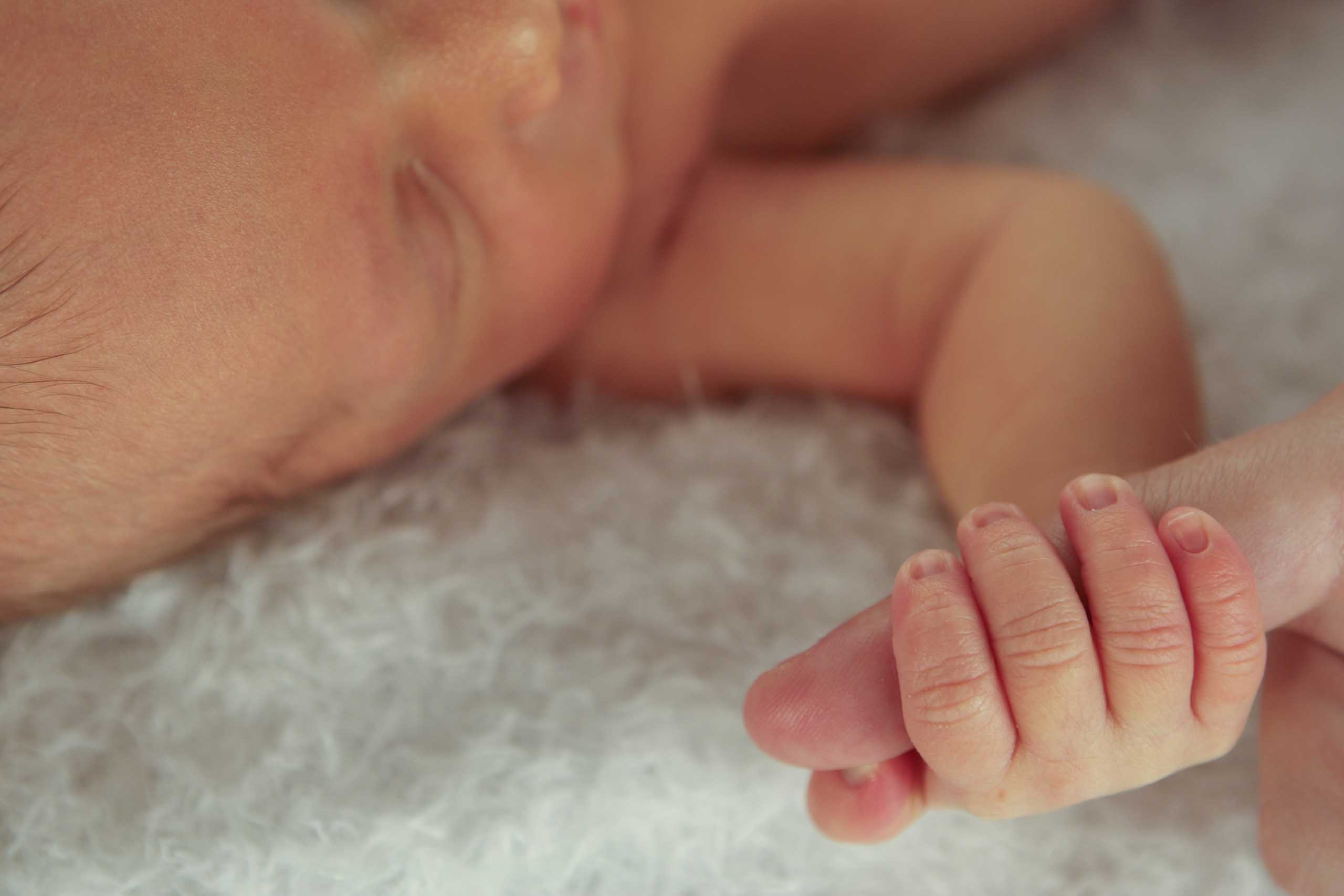 Premature baby with hand around adult thumb